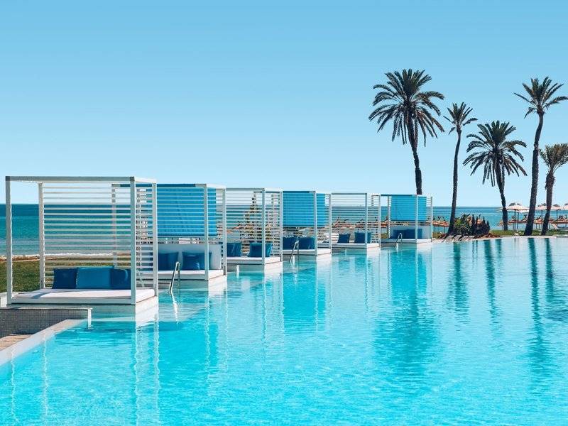 Ein blauer Pool mit Loungesesseln und Blick auf das Meer im Iberostar Selection Kuriat Palace.