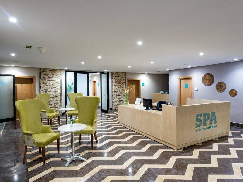 Empfangsbereich des Iberostar Selection Kuriat Palace Hotels mit SPA-Empfangstresen und grünen Stühlen.