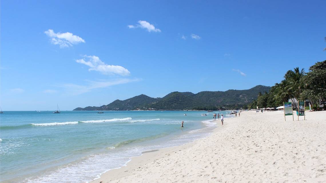 Strand des Banana Fan Sea Resorts mit weißen Sand, blauem Himmel und einigen Personen.