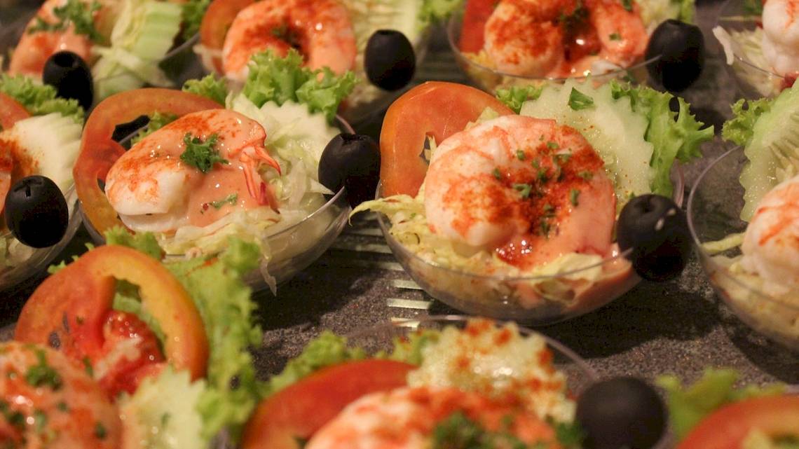 Eine Auswahl von Garnelensalate in kleinen Gläsern, dekoriert mit Tomatenscheiben und schwarzen Oliven.
