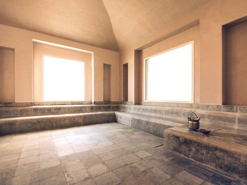 Eine leere Sauna im Iberostar Selection Diar El Andalous Hotel mit gefliesten Wänden und Boden, zwei großen Fenstern und einem kleinen Tisch.