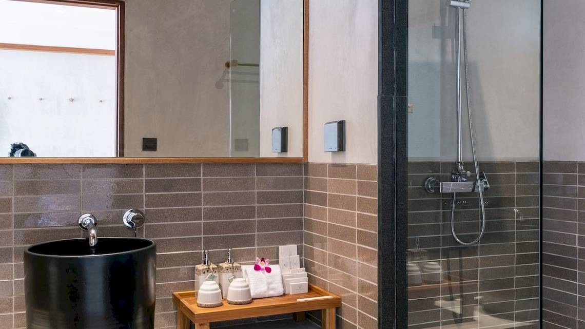 Badezimmer im Banana Fan Sea Resort mit einem schwarzen Waschbecken, einem Spiegel und einer Glasdusche.