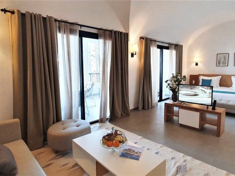 Hotelzimmer mit Schlafbereich, Couch, Tisch mit Obst und Fernseher auf einem Tisch neben dem Bett.