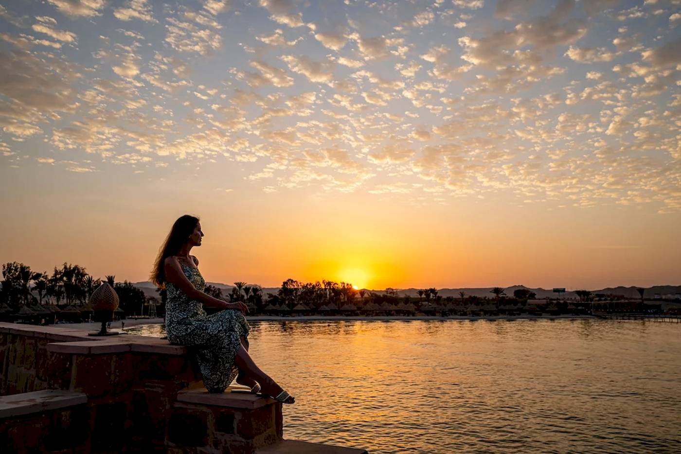 Eine Frau sitzt am Wasser während des Sonnenuntergangs im Mövenpick Resort El Quseir.