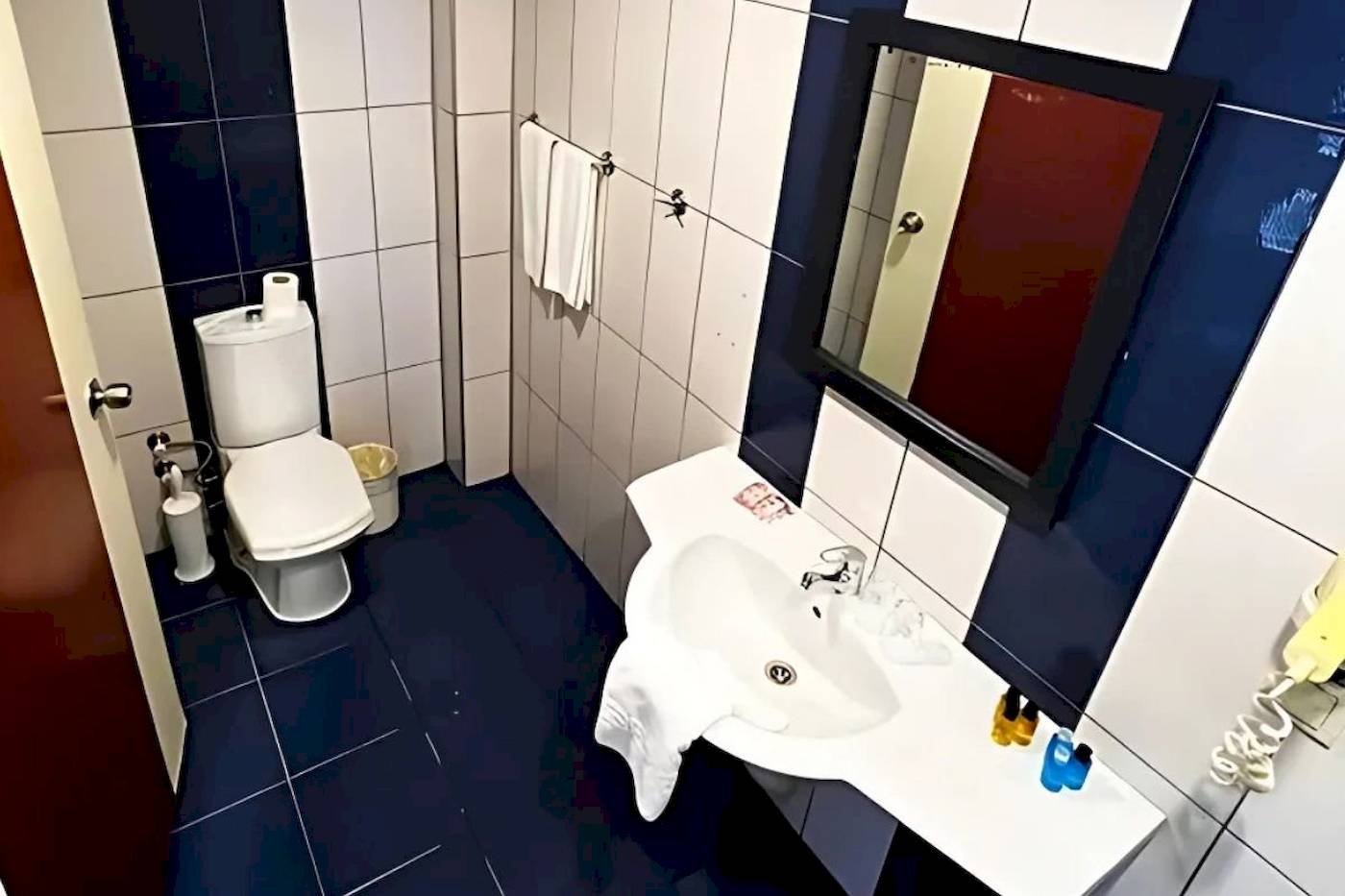 Badezimmer im Club Wasa Holiday Village mit weißer Toilette und blauen Fliesen.