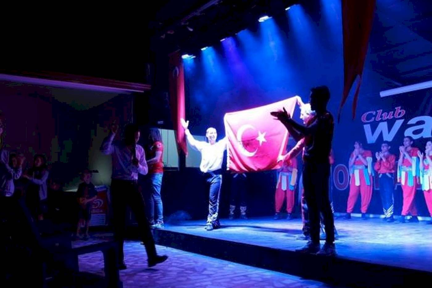 Feier auf der Bühne im Club Wasa Holiday Dorf mit einer Gruppe in roten Overalls, die eine türkische Flagge halten.