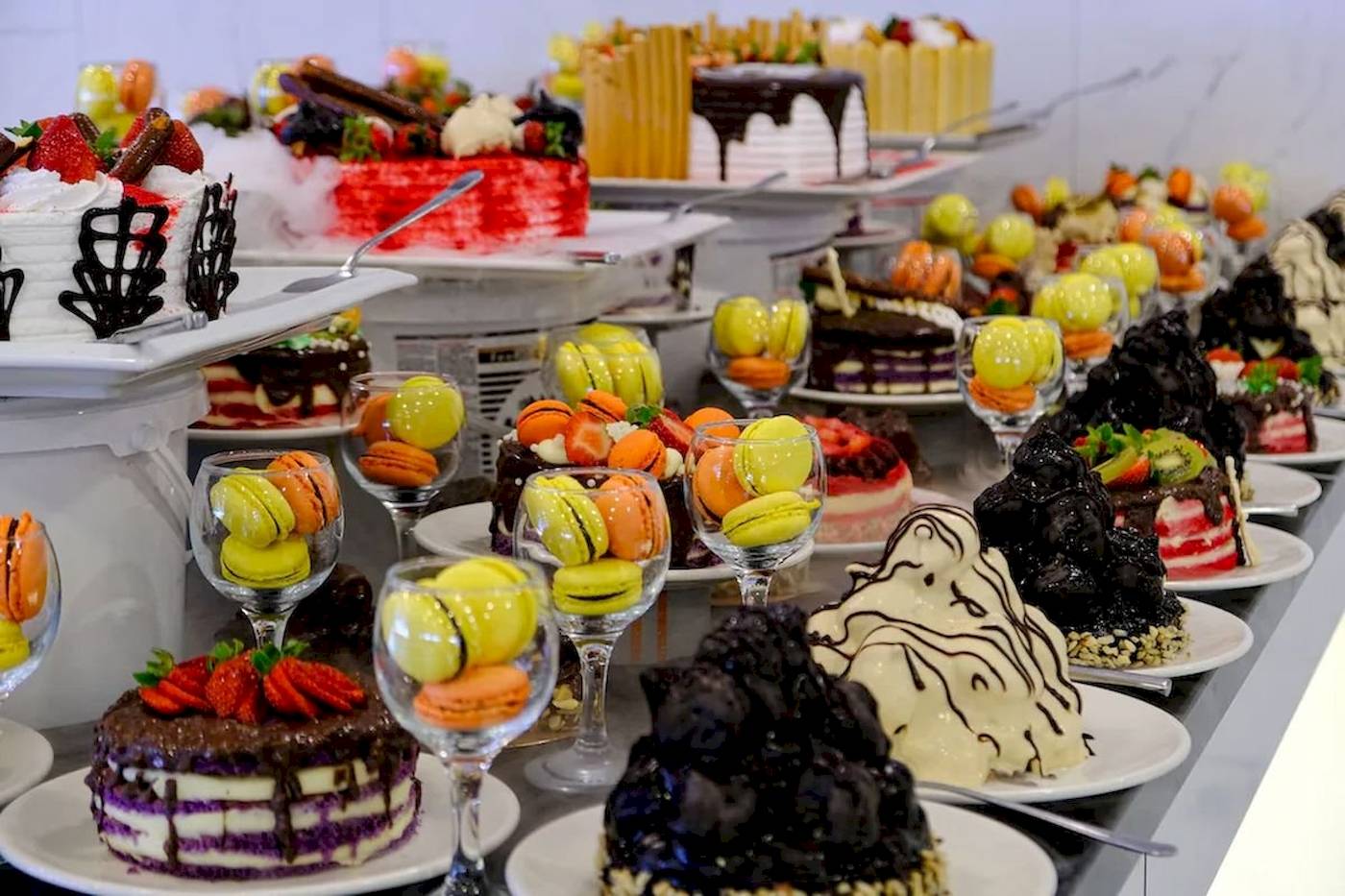 Club Wasa Holiday Village Kuchenbuffet mit verschiedenen Kuchen und Macarons auf weißen Tellern.