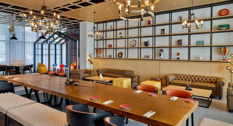 Innenbereich des NH Collection Dubai The Palm Hotels mit langen Holztischen, Stühlen, Couchen und dekorativen Gegenständen an den Wänden.