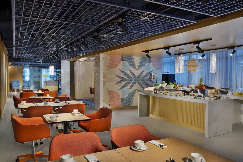 Innenansicht des Restaurants im NH Collection Dubai The Palm Hotel mit modernen Möbeln und einer großen Essenstheke.
