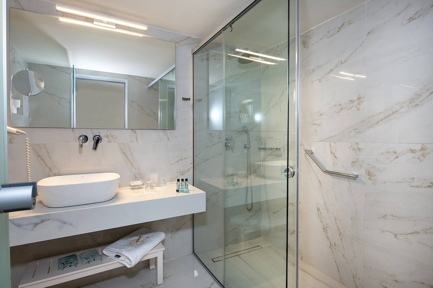 Vantaris Luxus Strandresort Badezimmer mit weißer Marmorwand und Glasdusche.