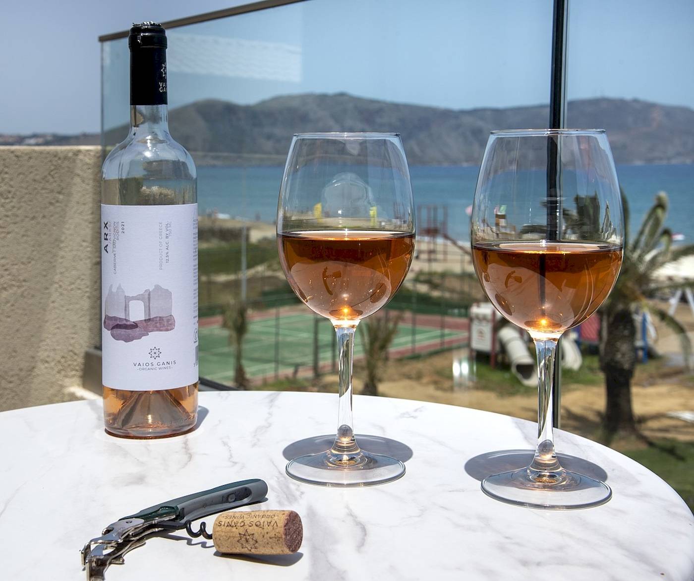 Eine Flasche Wein, zwei Gläser und ein Korkenzieher auf einem Tisch am Strand.