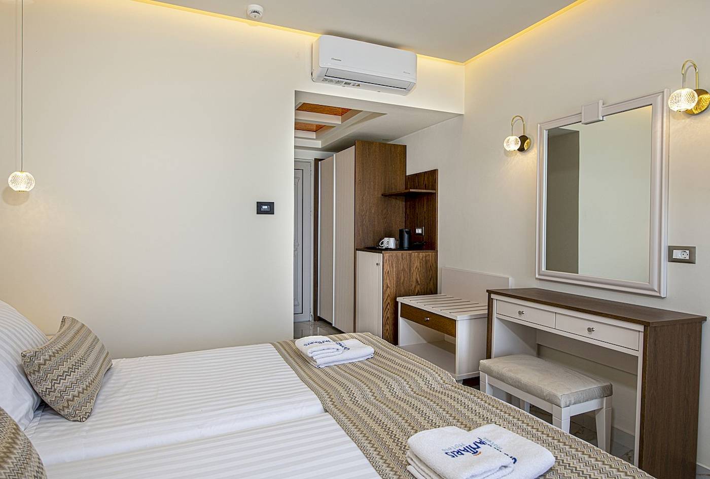 Interieur eines Hotelzimmers im Vantaris Luxury Beach Resort mit zwei Betten, Kleiderschrank und Klimaanlage.