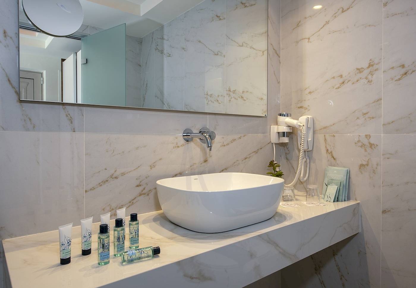 Badezimmer des Vantaris Luxury Beach Resort mit Marmorwänden, einem Waschbecken und Pflegeprodukten.