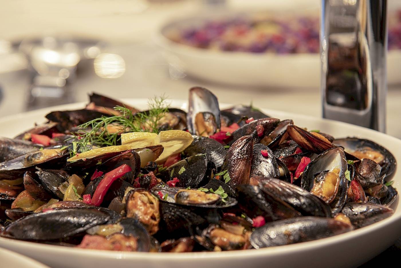 Eine Schüssel mit Muscheln, Paprika, Zwiebeln und Kräutern auf einem Tisch.