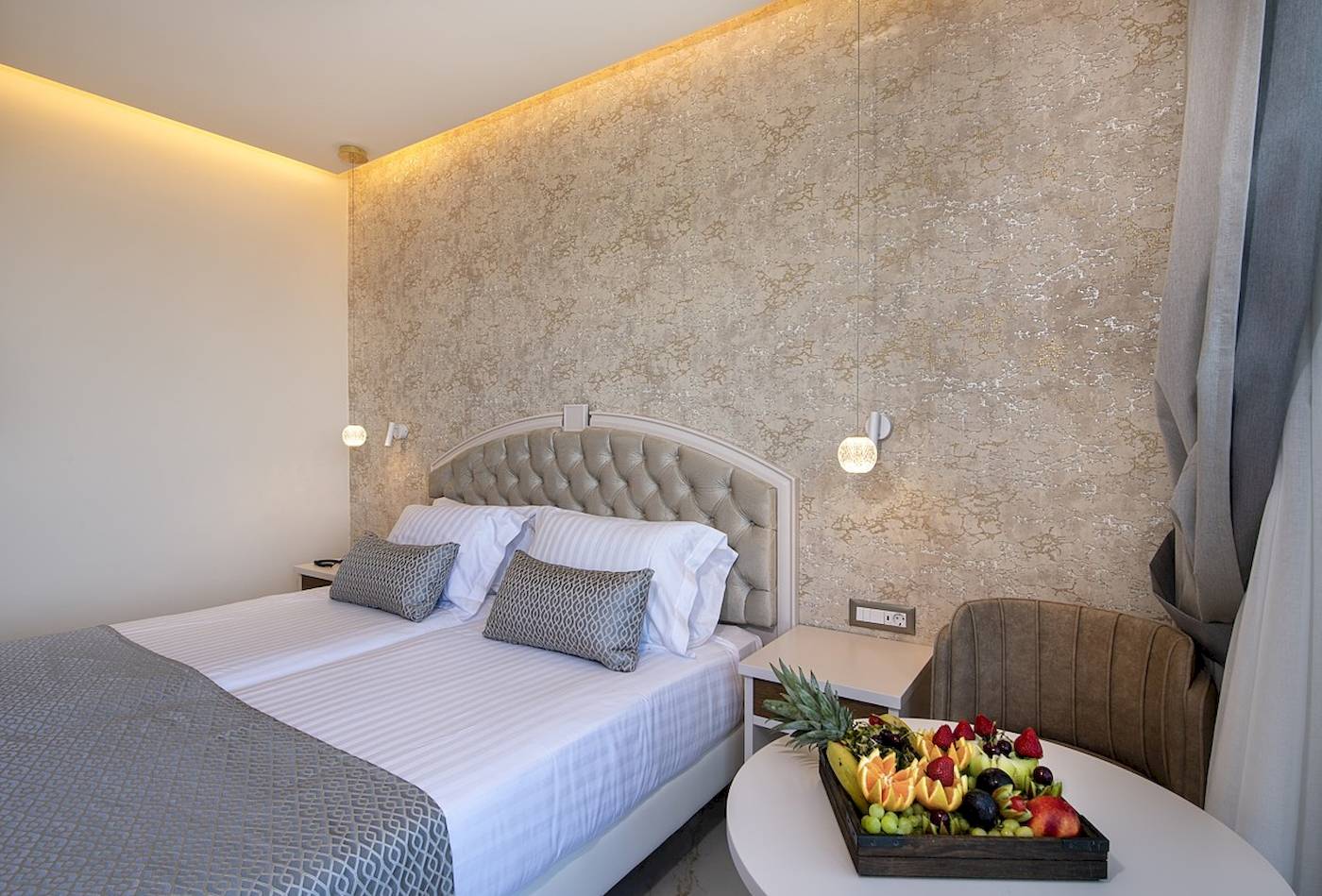 Hotelzimmer des Vantaris Luxury Beach Resort mit zwei Betten und einer Obstplatte auf dem Tisch.