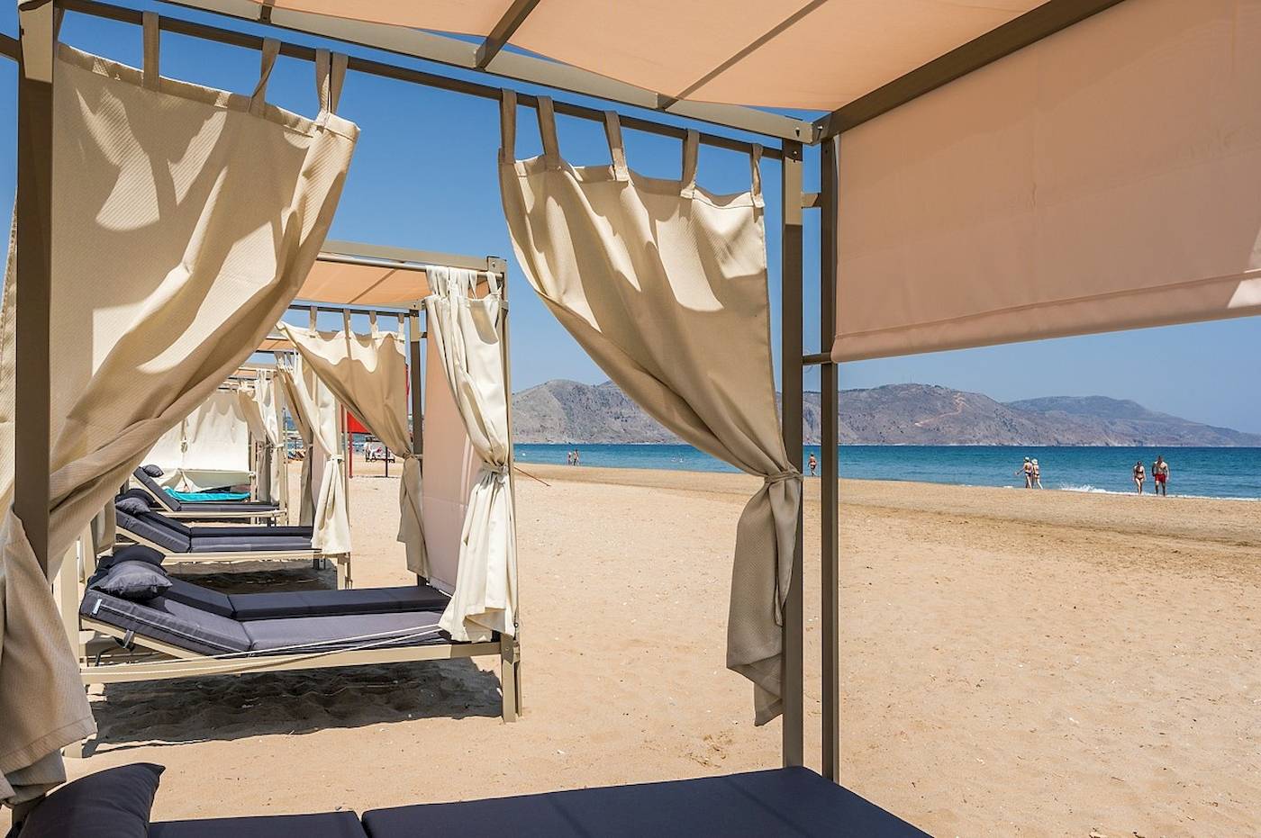 Sonnenliegen am Strand unter Pavillons am Vantaris Palace Hotel