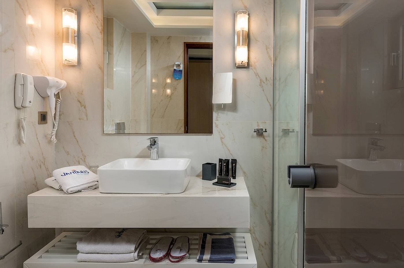 Badezimmer im Vantaris Palace Hotel mit Waschbecken, Handtüchern und Toilettenartikeln.