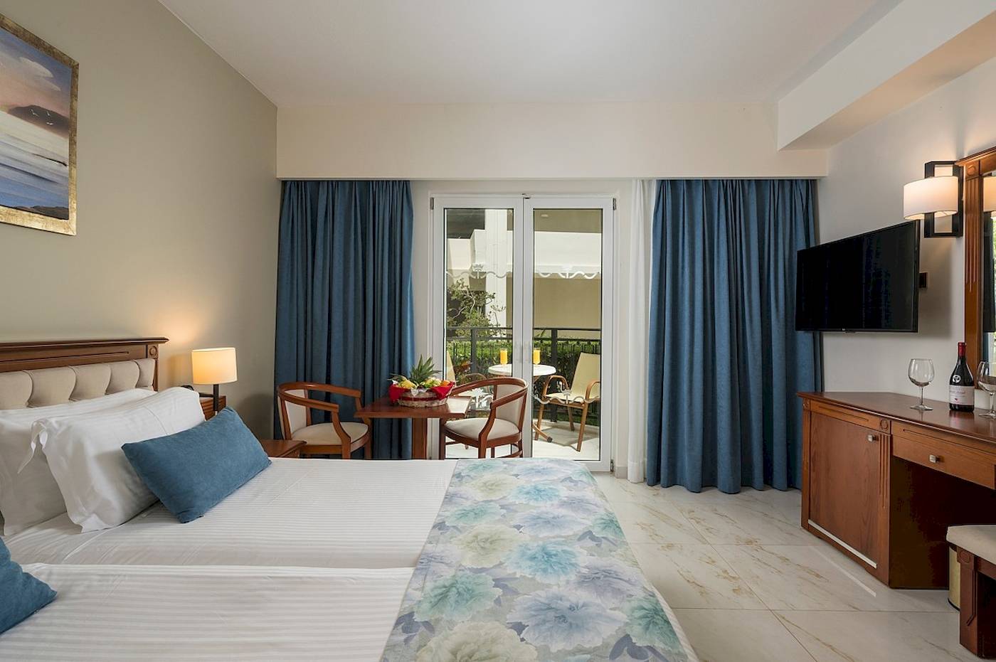 Innenansicht eines Schlafzimmers im Vantaris Palace Hotel mit zwei Betten, Tisch, Stühlen und Balkon.