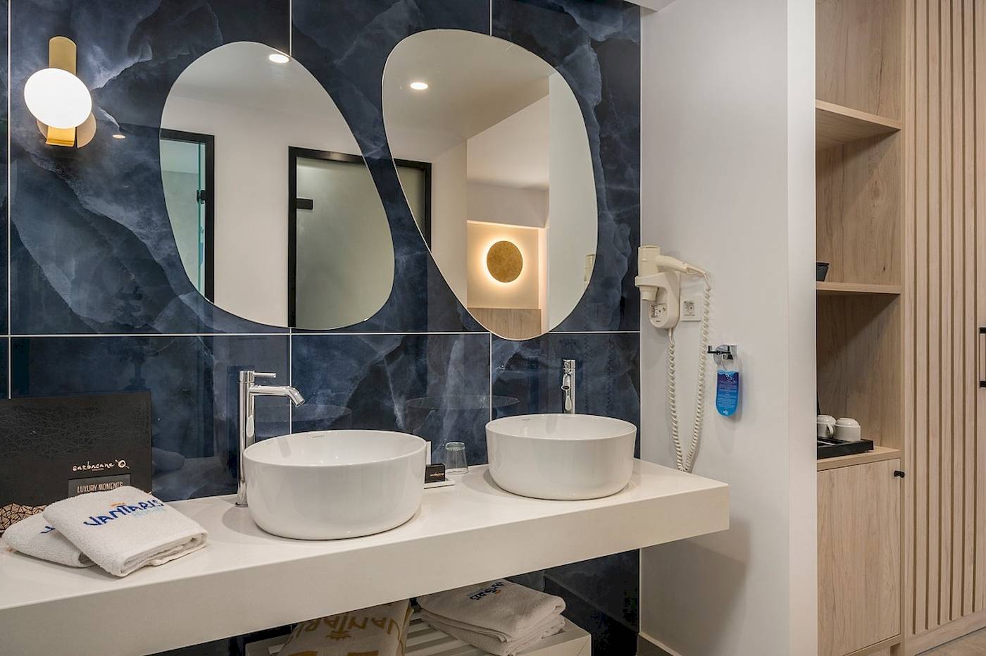 Badezimmer im Vantaris Palace mit zwei Waschbecken, Spiegeln und blauer Wandgestaltung.