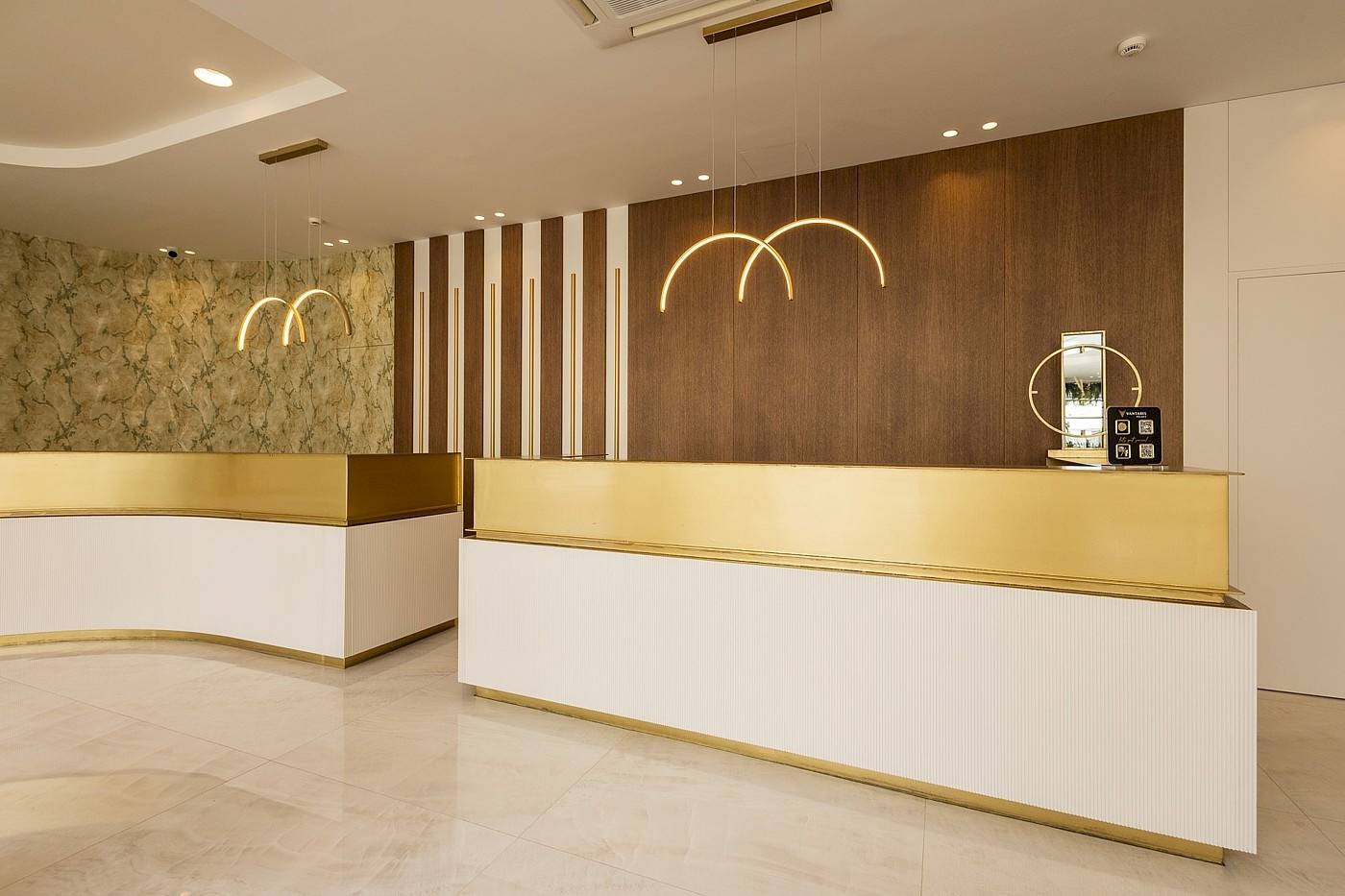 Empfangsbereich des Vantaris Palace Hotels mit goldfarbener Theke und dekorativen Kronleuchtern.