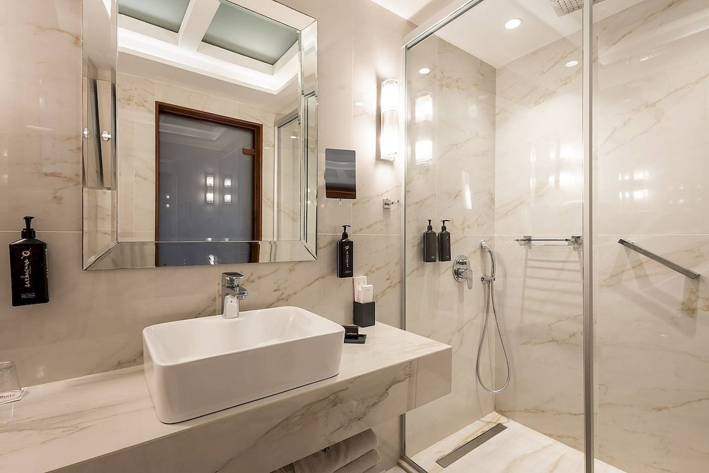 Badezimmer im Vantaris Palace mit Marmorfliesen, Dusche und Waschbecken.