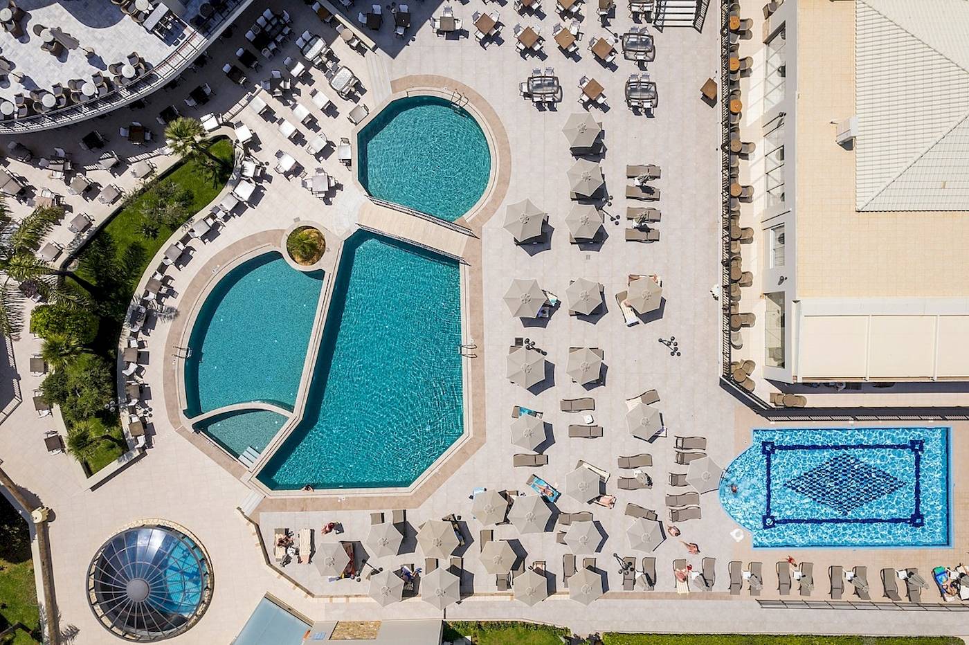 Luftaufnahme des Vantaris Palace Schwimmbadbereichs mit mehreren Pools und Sonnenliegen.