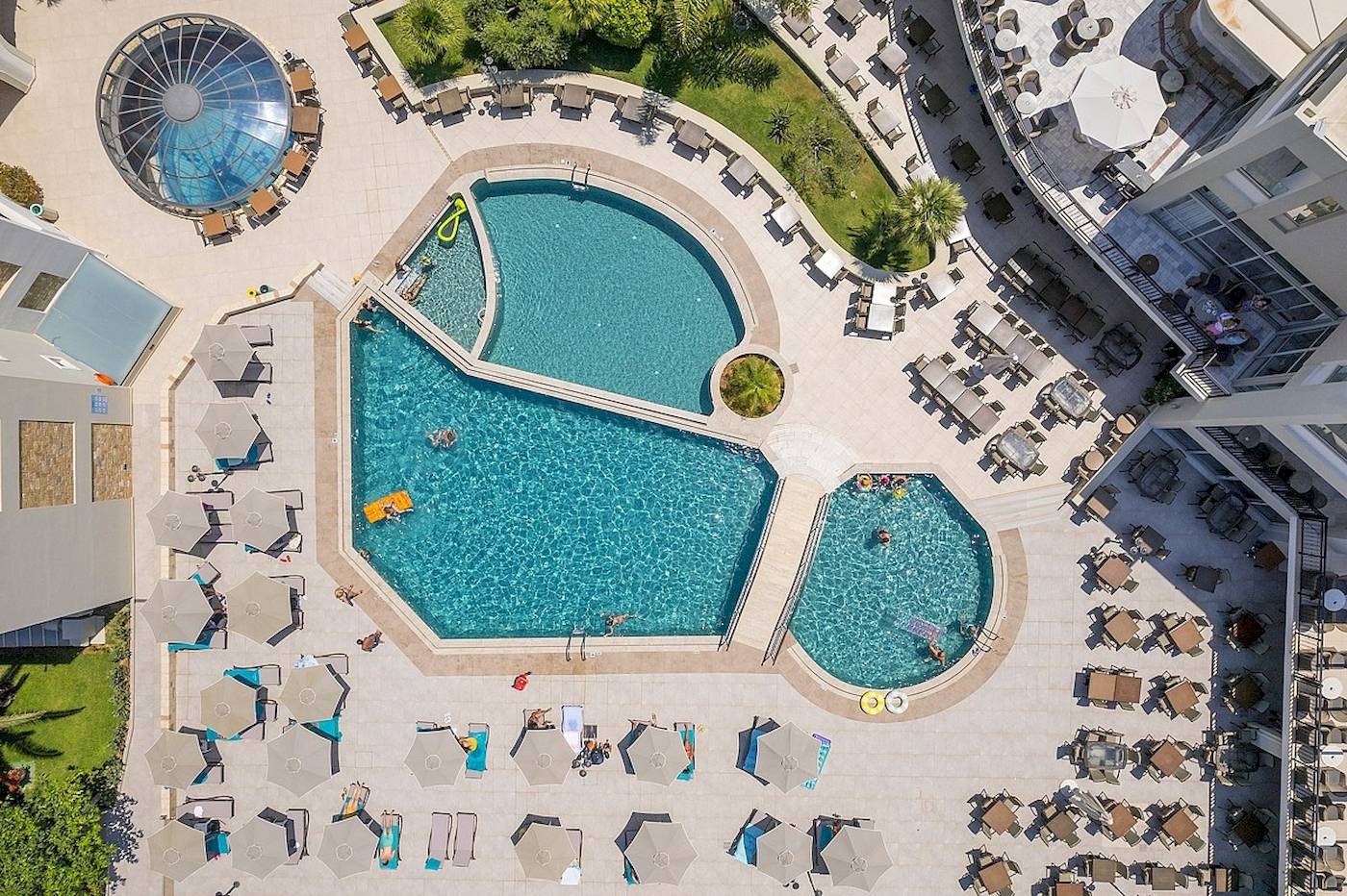 Luftaufnahme des Vantaris Palace mit Swimmingpools, Sonnenliegen und Schirmen.