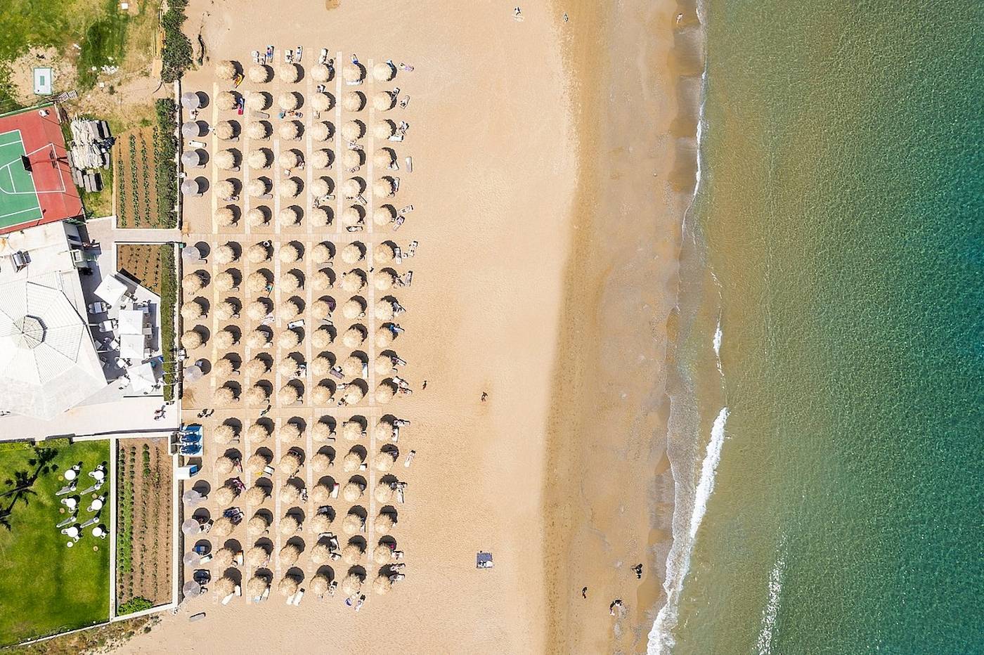 Oberflächenansicht eines Strandes mit vielen Sonnenhüten und einem Hotelgebäude im Hintergrund.