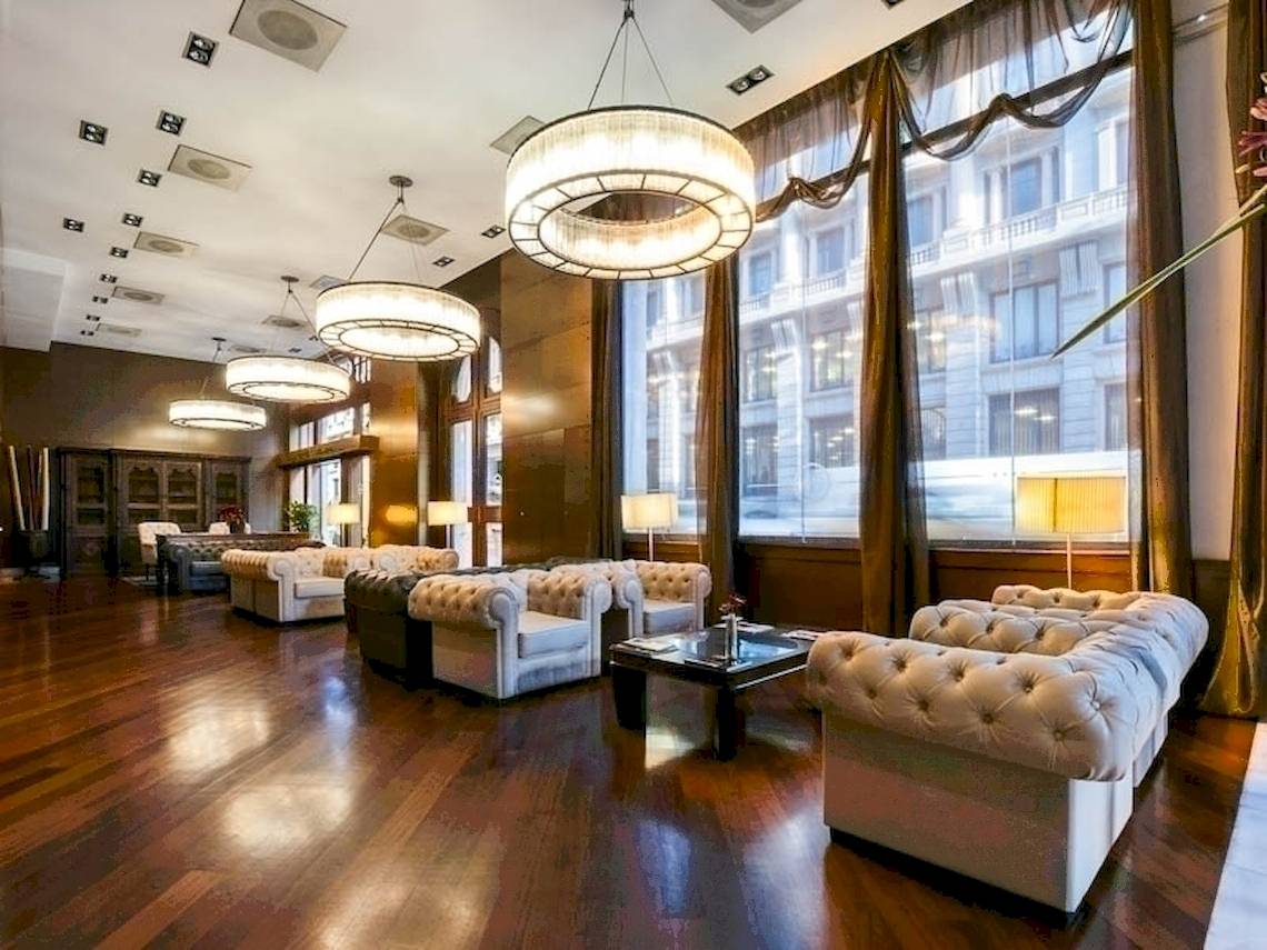 Lobby des Colonial Barcelona Hotels mit weißen Sofas, Holzboden und großen Kronleuchtern.