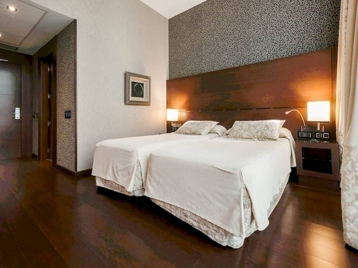 Schlafzimmer im Colonial Barcelona Hotel mit zwei Betten, Nachttischen und Lampen.