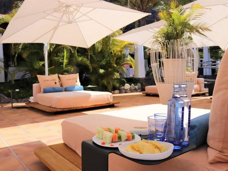 Gartenlounge-Bereich im Jardin Tecina Hotel mit einem Bett unter einem Schirm und einem Tablett mit Essen und Getränken.