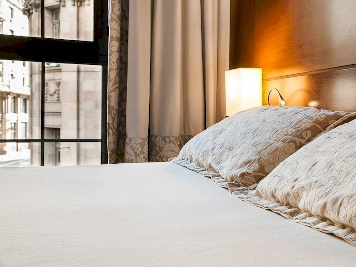 Bett im Colonial Barcelona Hotel mit Kissen und Fenster mit Stadtblick