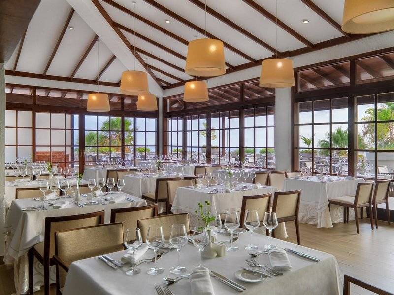 Innenbereich des Jardin Tecina Hotels mit mehreren gedeckten Tischen und Stühlen, umgeben von großen Fenstern.