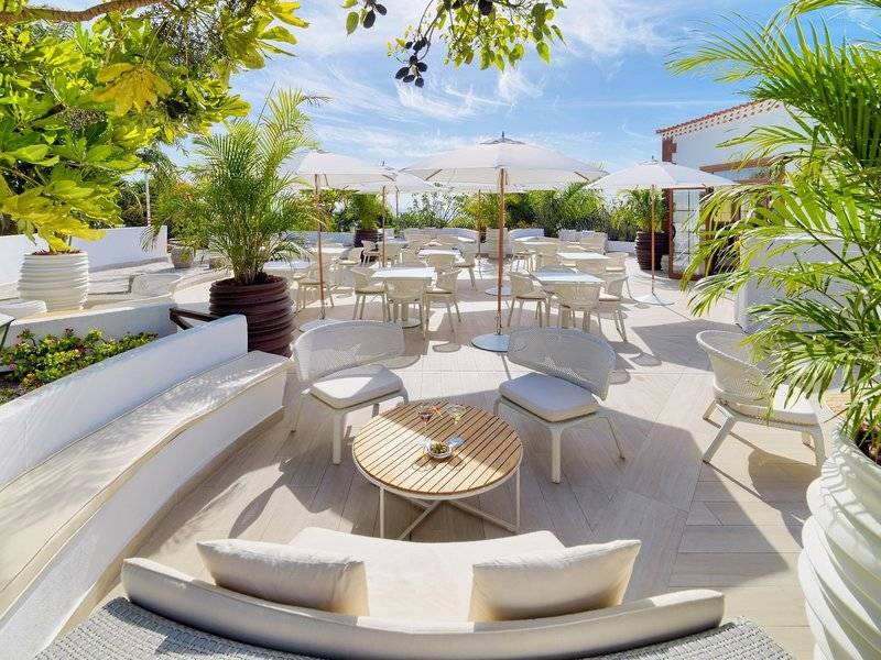 Garten Terrasse des Hotels Jardin Tecina mit weißen Tischen und Stühlen, Sonnenschirmen und Pflanzen.