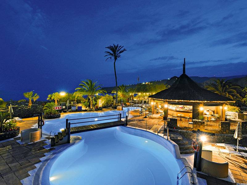 Ein abendlicher Blick auf den Pool des Jardin Tecina Hotels mit beleuchteter Bar und umgebenden Palmen.