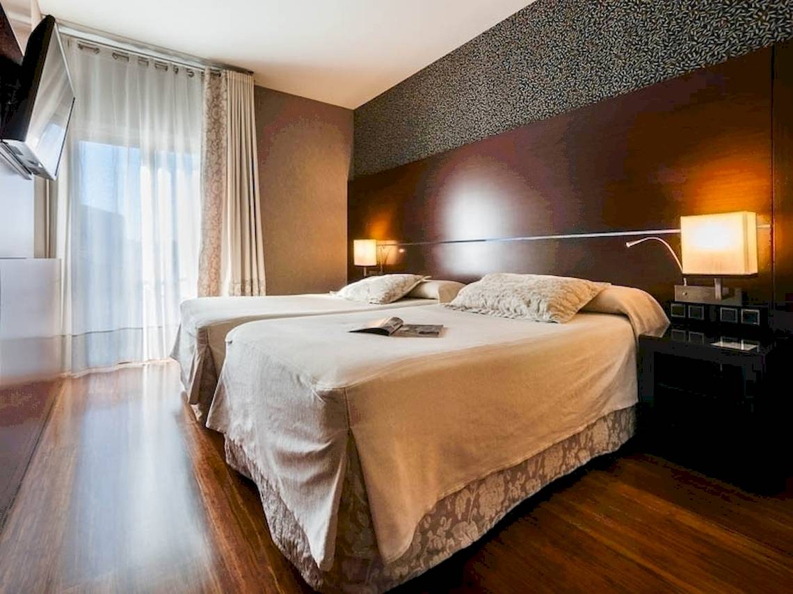 Doppelbettzimmer im Colonial Barcelona Hotel mit Holzboden und gemusterten Wänden.