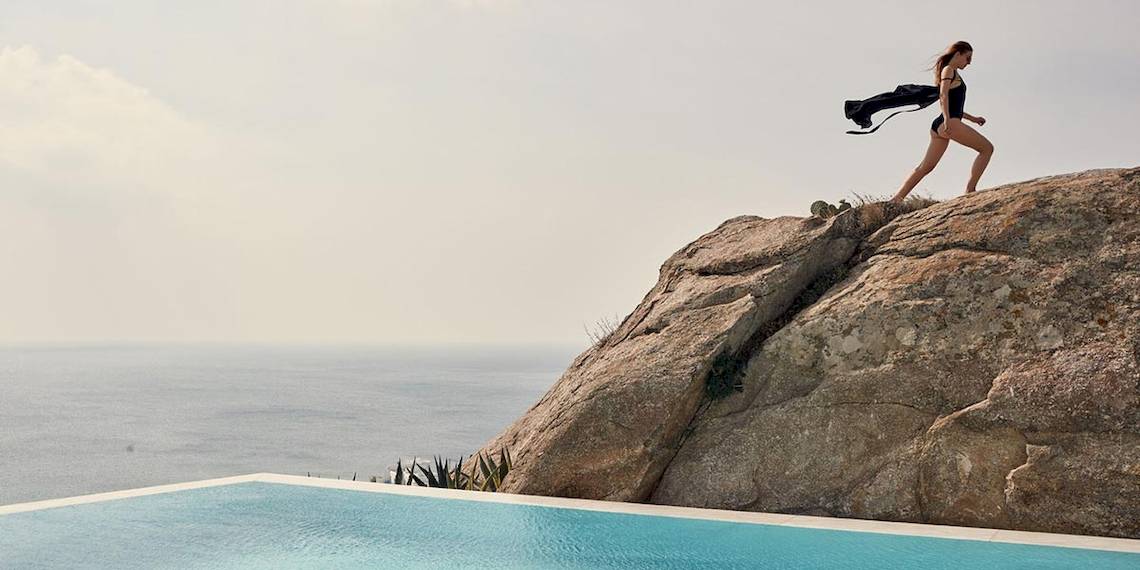 Frau in Badeanzug steht auf Felsen am Pool des Myconian Ambassador Hotels