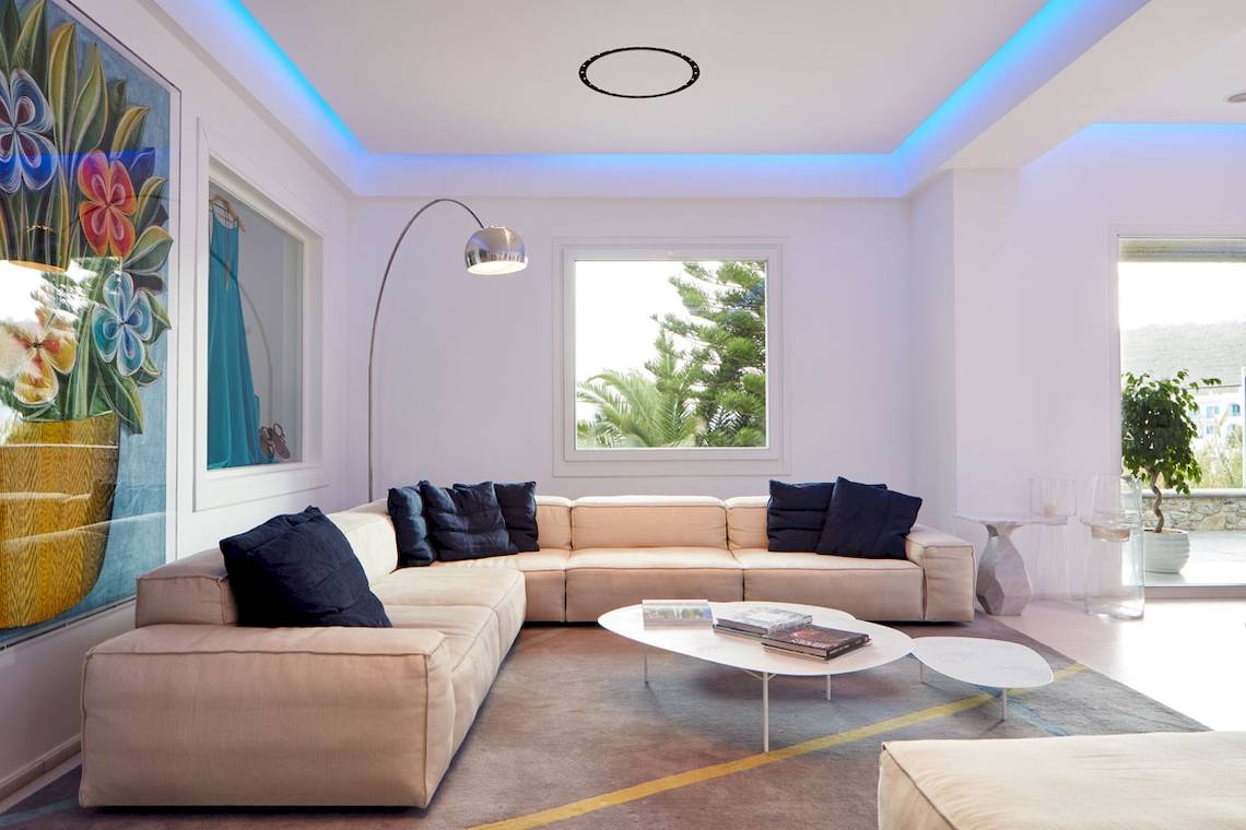 Wohnzimmer im Myconian Ambassador Relais & Chateaux Hotel mit Couch, Couchtisch und Lampe.