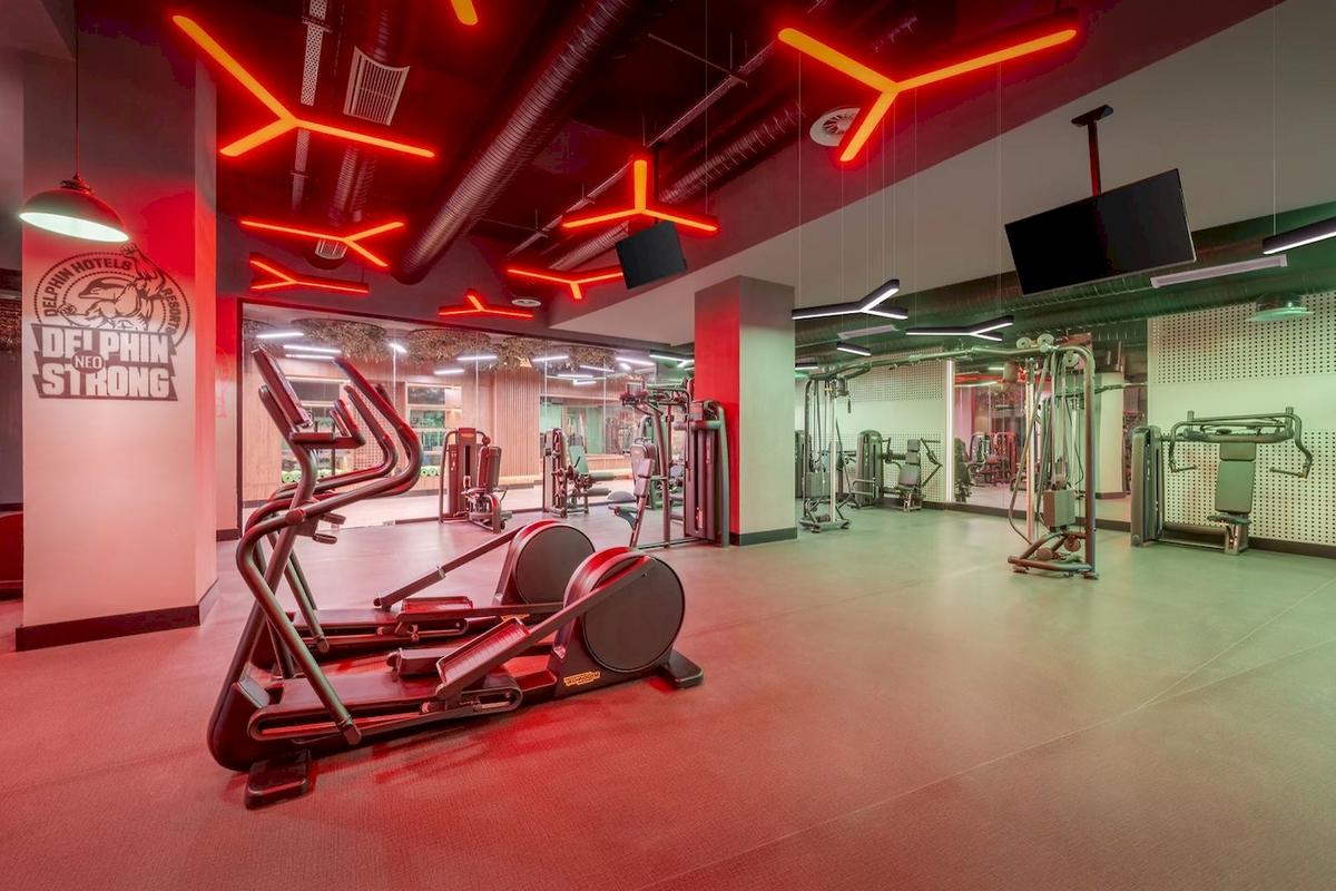 Innenansicht des Fitnesscenters im Delphin Palace Hotel mit roter Beleuchtung und Fitnessgeräten.