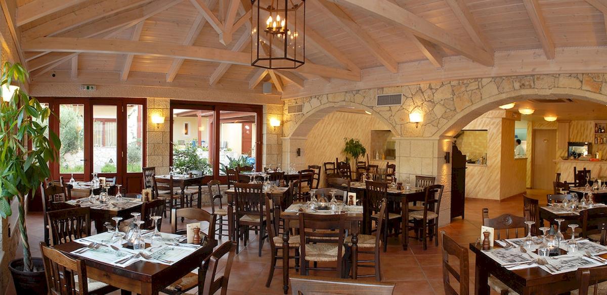 Innenansicht des Restaurants im Cactus Village Hotel mit Holztischen, Stühlen und einem hängenden Kronleuchter.
