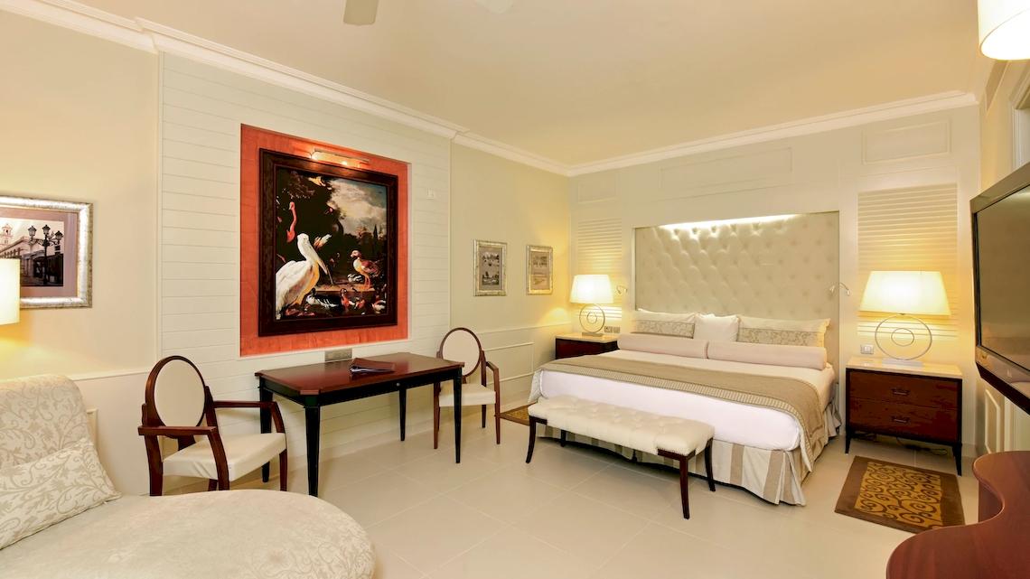 Suite-Schlafzimmer im JOIA Bávaro by Iberostar mit Doppelbett, Schreibtisch und Stühle.