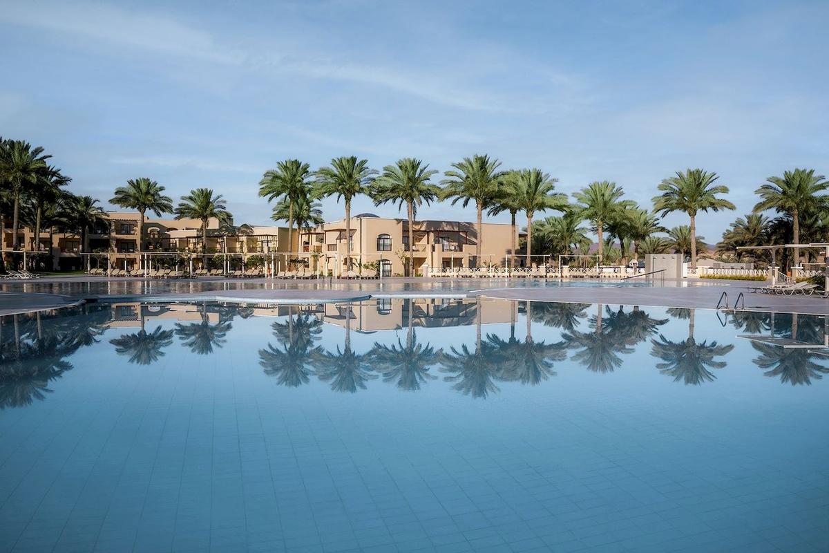 Außenpool des Jaz Lamaya Resorts mit Palmen und Hotelgebäuden im Hintergrund.