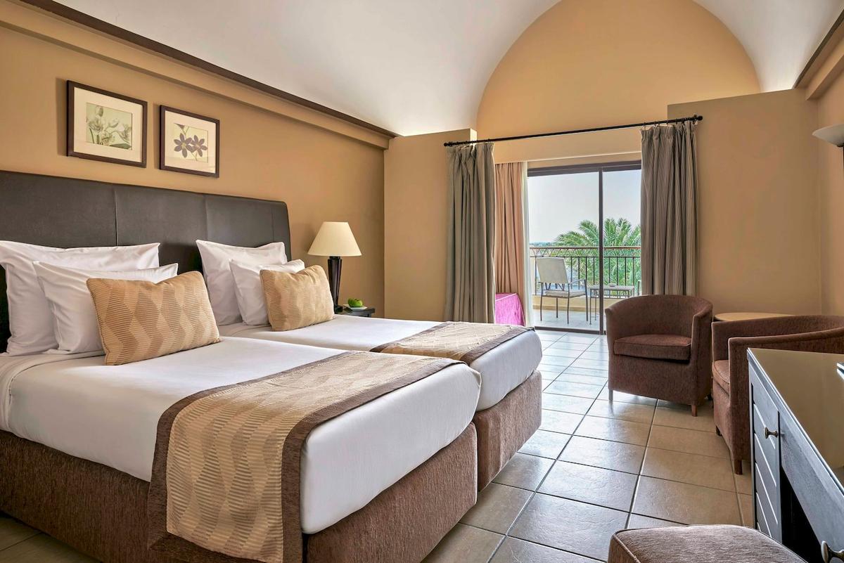Doppelzimmer im Jaz Lamaya Resort mit zwei Betten, Sessel, Schreibtisch und Balkon mit Meerblick.
