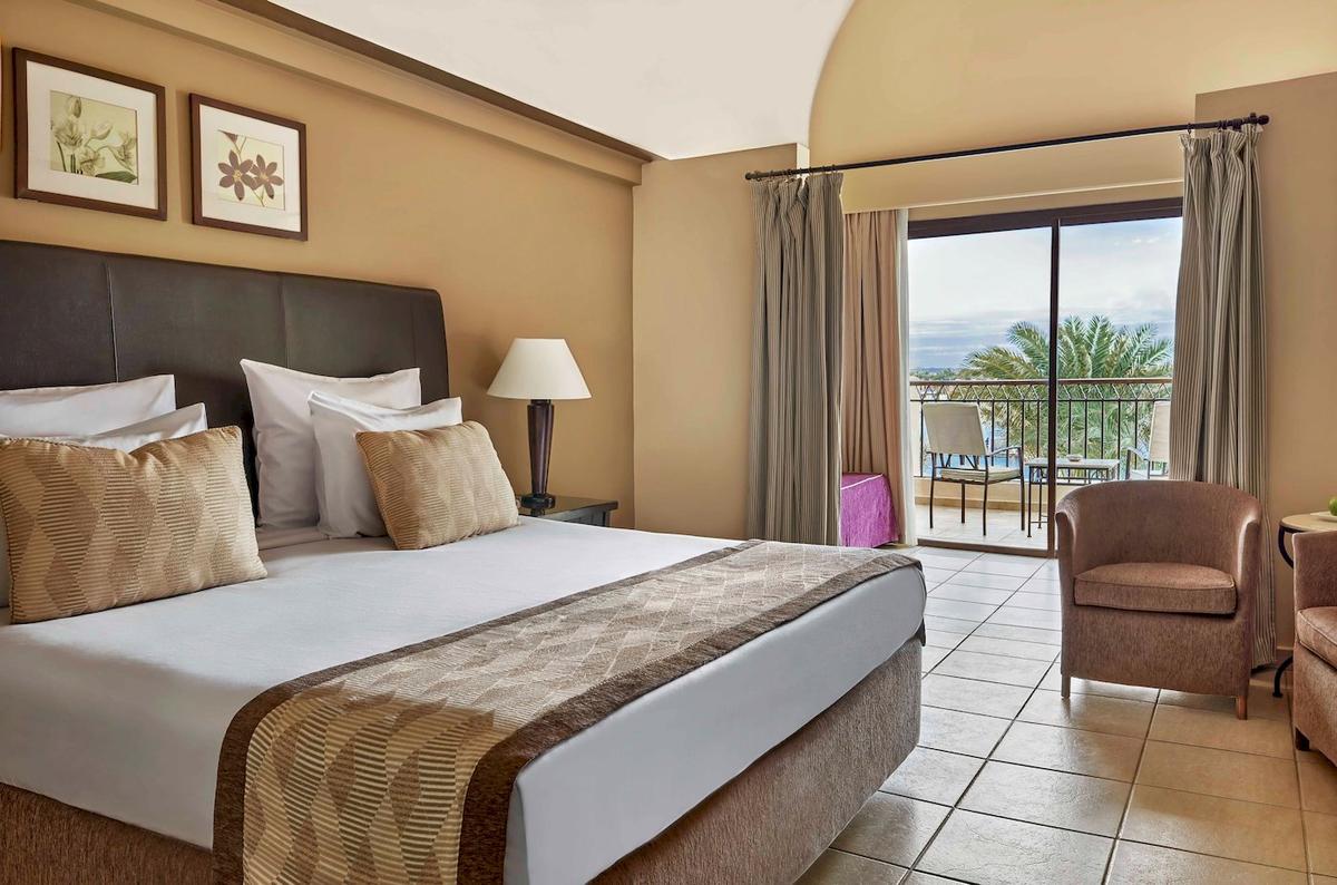 Doppelzimmer im Jaz Lamaya Resort mit Bett, Kissen, Nachttisch, Lampe und Balkon.