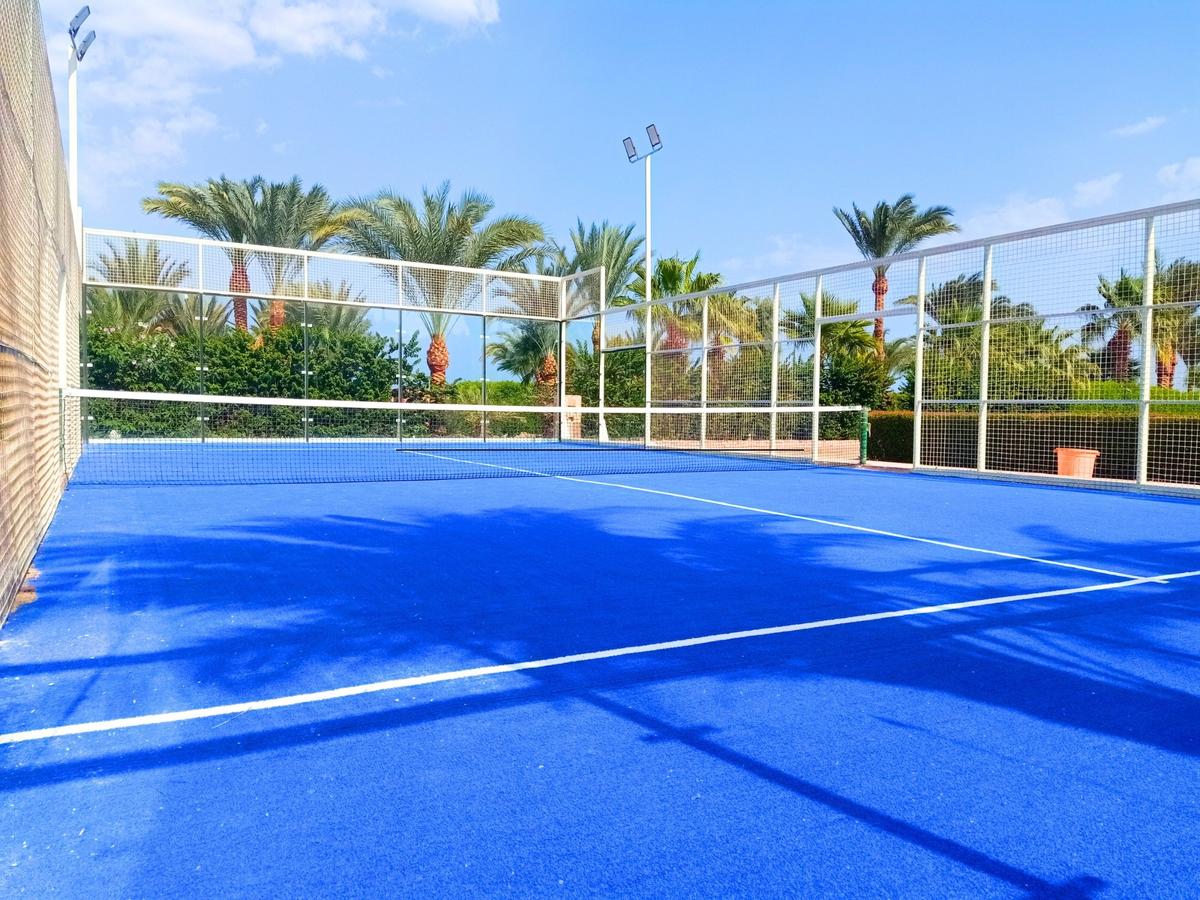 Ein leerer Tennisplatz des Utopia Beach Club mit blauem Boden und hohen Palmen im Hintergrund.