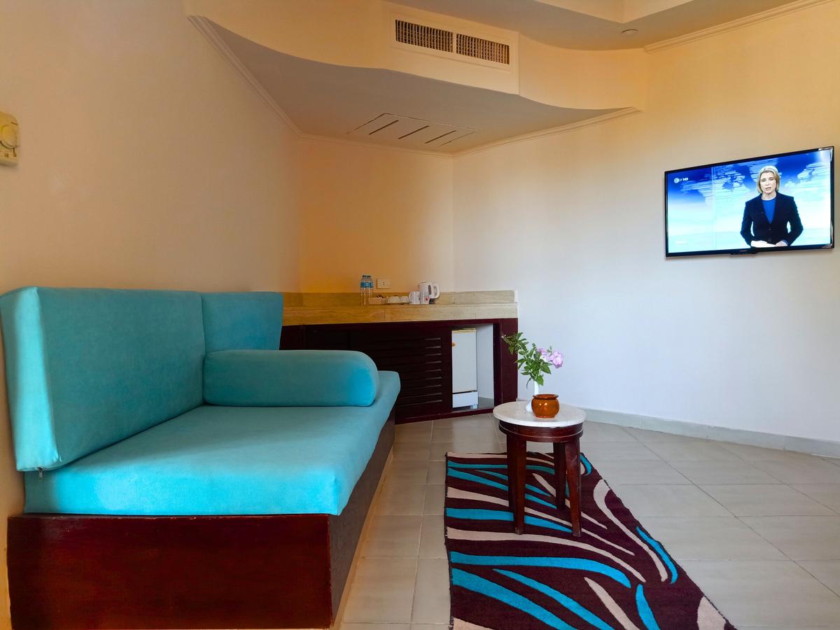 Wohnbereich im Utopia Beach Club Hotel mit blauem Sofa, Tisch, Fernseher und Blumen.