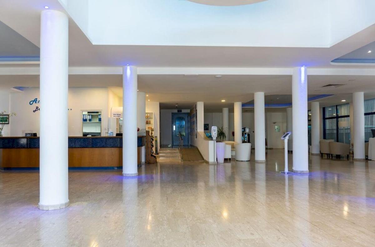 Lobby des Anonymous Beach Hotels mit Empfangstresen, weißen Säulen und Sitzbereich.
