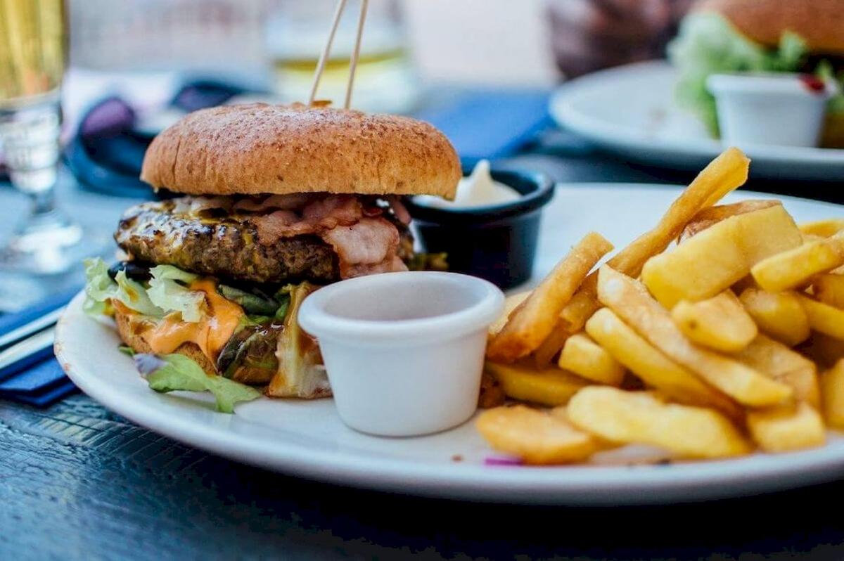Ein Burger mit Pommes Frites auf einem weißen Teller, serviert mit einer Tasse Ketchup.