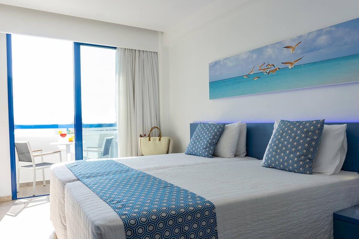 Doppelzimmer mit Meerblick im Anonymous Beach Hotel, mit zwei Betten, blauen Kissen und einem großen Wandbild von fliegenden Vögeln.