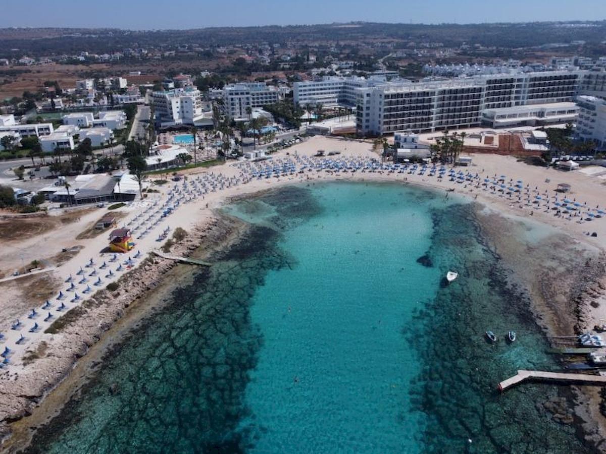 Luftaufnahme des Anonymous Beach Hotels, das an einen Strand angrenzt mit vielen Sonnenliegen und blauem Wasser.